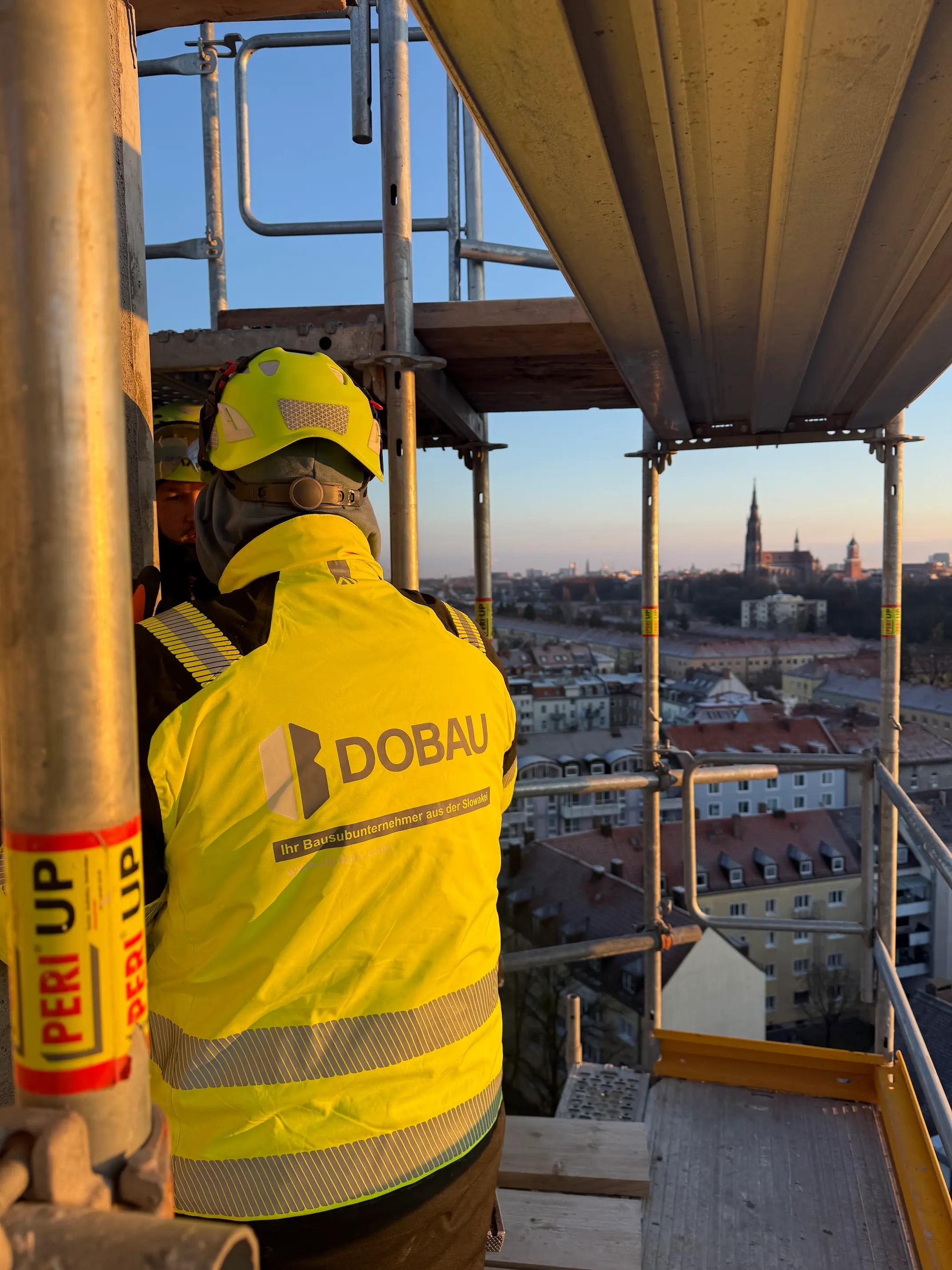 Pracovník v bezpečnostnej prilbe na lešení s výhľadom na mesto